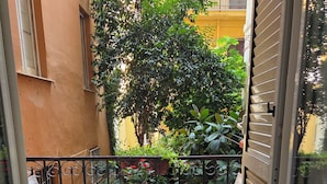 A small balcony with two chairs and a table, surrounded by potted plants and a red rug. - Napoli SottoSopra a Chiaia, Elegant central apartment for groups and families (Napoli)