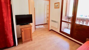 A room with a television on a wooden stand, a radiator, and a window with a view of a balcony.