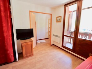 Una habitación con una televisión sobre un soporte de madera, un radiador y una ventana con vistas a un balcón.