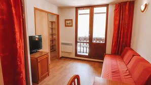 A living room with a TV, a red sofa, a wooden table, and a balcony with red curtains.