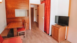 A compact room with a wooden dining table, a TV on a wooden cabinet, and a red curtain.