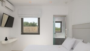 A modern bedroom with a large bed, a mounted TV, a window, and a bathroom visible through an open door. - Ivory Villa, Heated Pool, Hot Tub, Sauna & Gym (Perama)