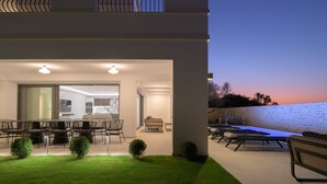 A modern outdoor patio with a dining area, lounge chairs, and a swimming pool. - Ivory Villa, Heated Pool, Hot Tub, Sauna & Gym (Perama)