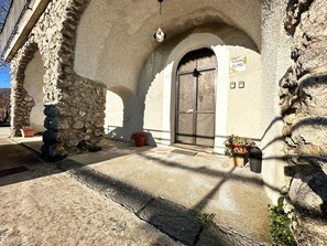 A stone building with a large wooden door, a sign reading "DIMORA ALMA", and potted plants outside.