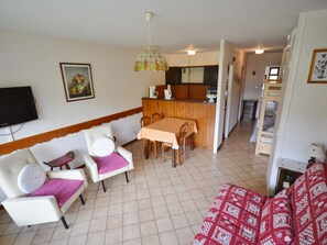 Una sala de estar con sofá, una mesa de comedor con sillas, una zona de cocina y un televisor montado en la pared.