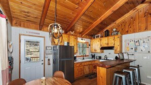 Una cocina rústica con armarios de madera, una isla central con taburetes, un refrigerador y una mesa de comedor.
