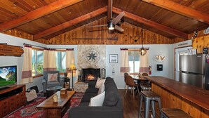 Interior rústico de una cabaña con chimenea, techo de madera y una zona de comedor.
