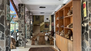 A spacious room with a stone wall, wooden benches, and a large wooden cabinet filled with decorative items. - Omah Eling Medang Kamulan Borobudur (Borobudur)