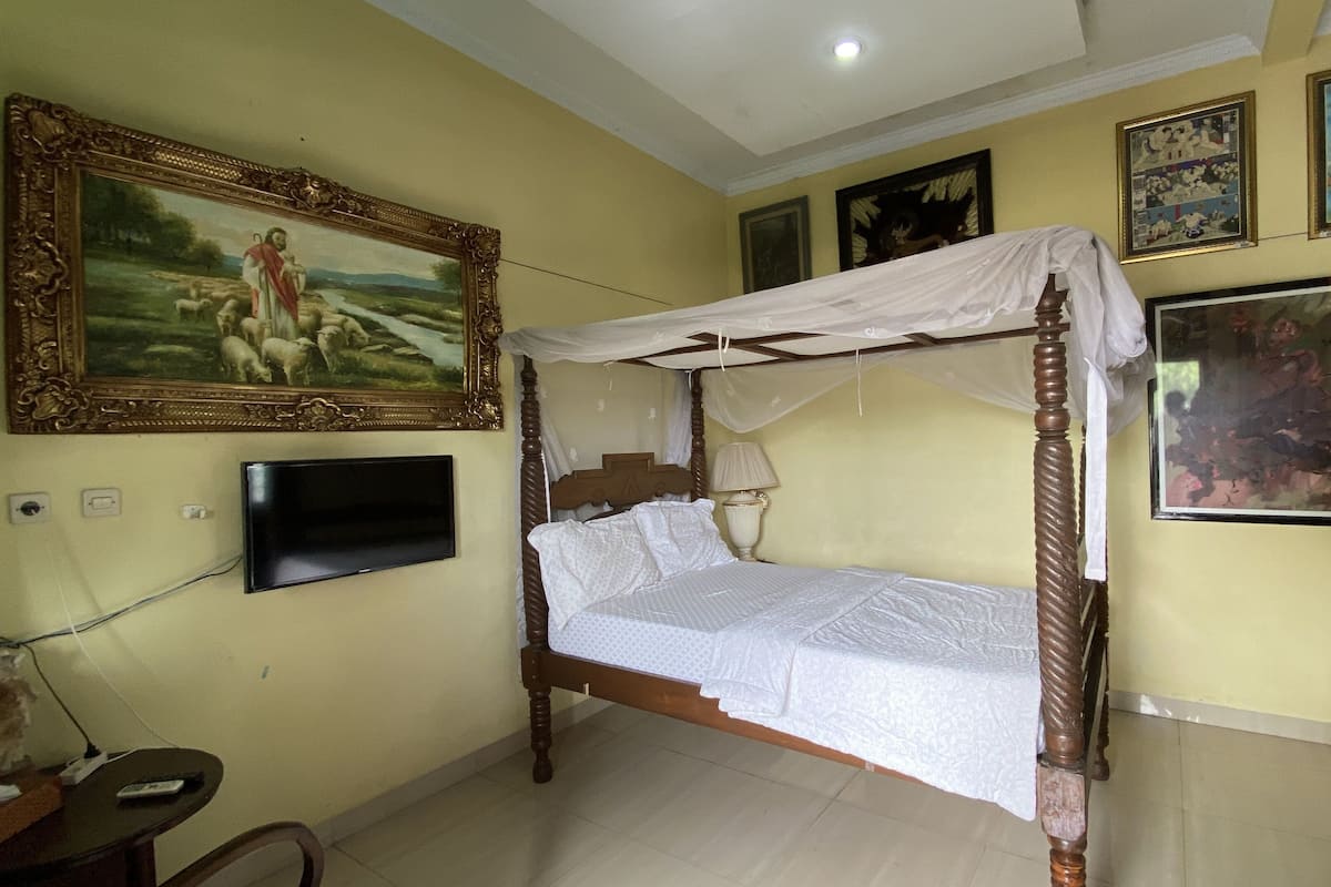 A bedroom with a four-poster bed, a television on the wall, and various framed artworks.