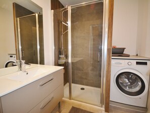 A modern bathroom with a glass-enclosed shower, a built-in washing machine, and a vanity with a mirror.