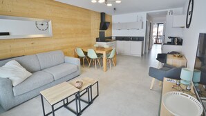 Een moderne woonkamer met een grijze bank, een houten salontafel, en een eethoek met een houten tafel en stoelen.