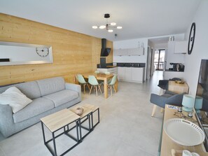 A modern living room with a grey sofa, a wooden coffee table, and a dining area with a wooden table and chairs. - Modern Apartment for 6, Steps from Pleney Slopes, Balconies, Wi-Fi (Morzine)