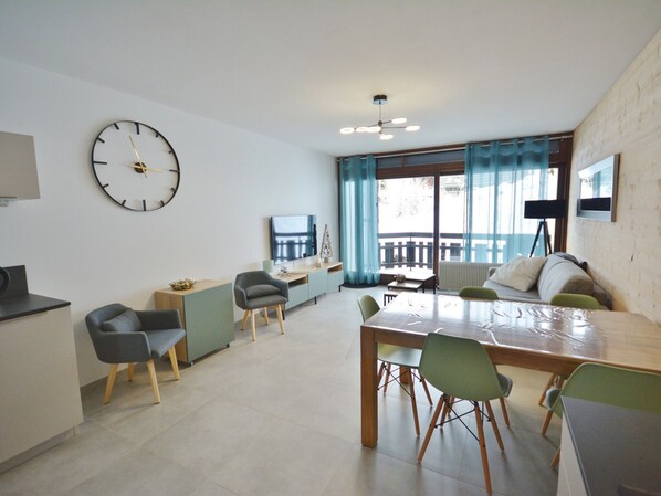A modern living room with a dining area, a large clock on the wall, and a balcony with curtains.
