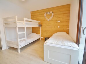 A room with bunk beds and a single bed, wooden walls, and a heart-shaped decoration. - Modern Apartment for 6, Steps from Pleney Slopes, Balconies, Wi-Fi (Morzine)