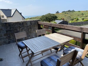 Um pátio com mesa e cadeiras, um muro de pedra e vista para uma paisagem montanhosa.
