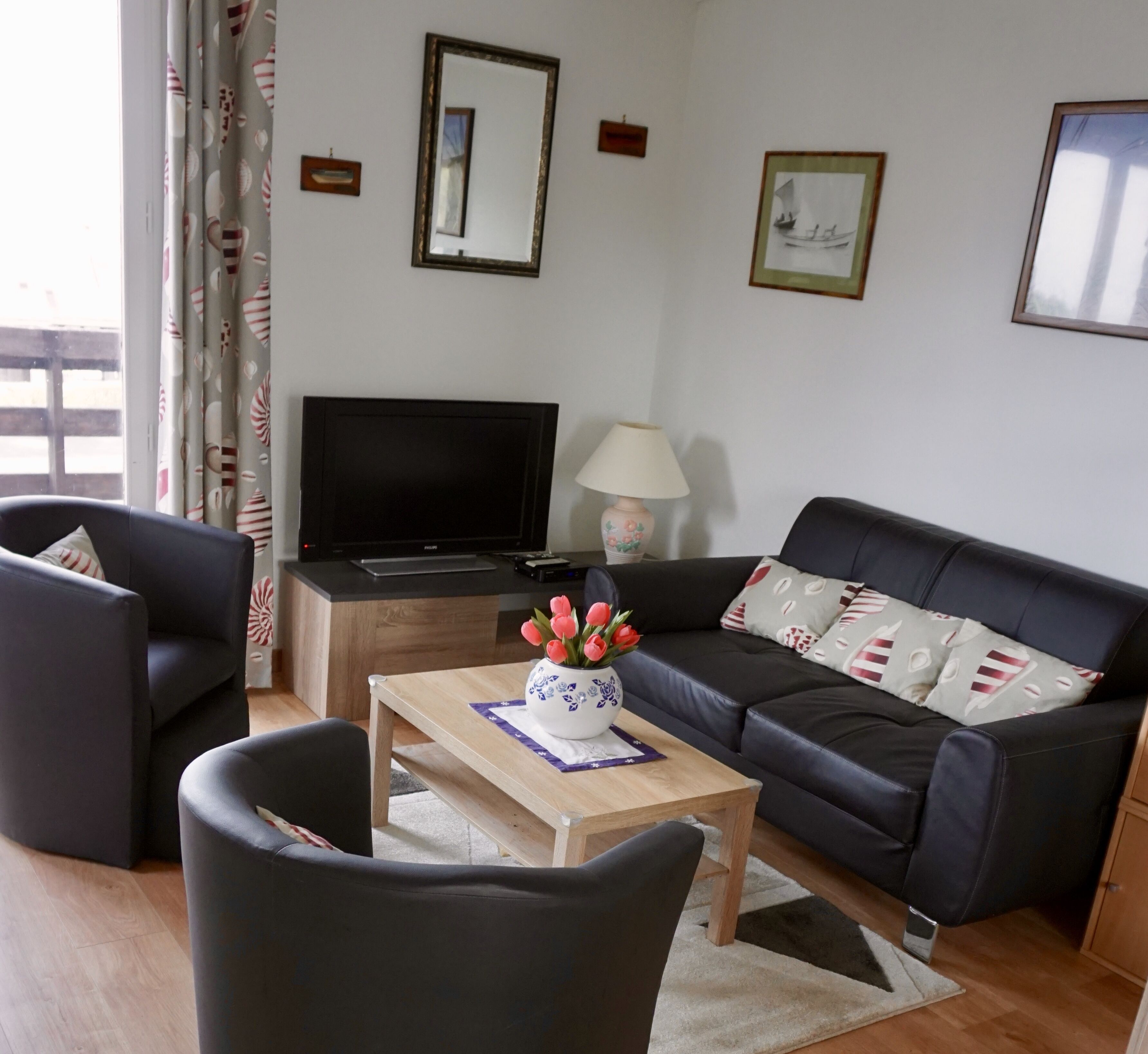 Ein Wohnzimmer mit einer schwarzen Couch, einem Holztisch, einem Fernseher und einer Lampe.