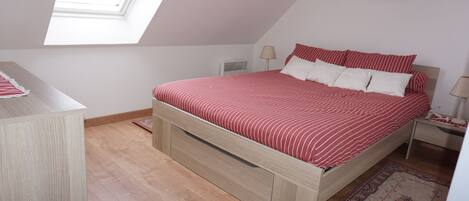 A bedroom with a sloped ceiling, a bed with red and white bedding, a wooden nightstand, a lamp, and a small rug.