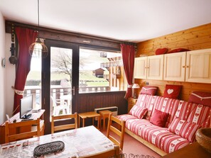 A cozy room with a wooden ceiling, a red and white striped sofa, a wooden table with chairs, and a window with curtains.