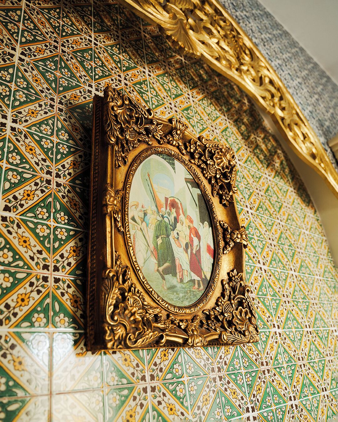A framed picture with ornate gold detailing on a tiled wall.