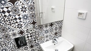 A bathroom with a white toilet, a white sink, and a mirror above the sink. The walls are tiled with a black and white pattern. - Bit HSAN :Original guestroom (Mahdia)
