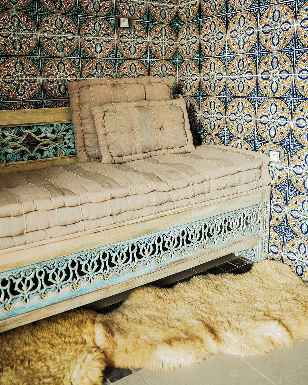 Un lit doté d’une tête de lit capitonnée et d’un cadre décoratif en métal, placé contre un mur recouvert de carreaux à motifs.