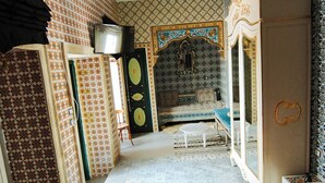 A room with patterned walls, a chandelier, a bed, a mirror, and a television. - Bit HSAN :Original guestroom (Mahdia)