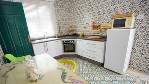 A small kitchen with a green door, white cabinets, a stove, and a microwave. - Bit HSAN :Original guestroom (Mahdia)