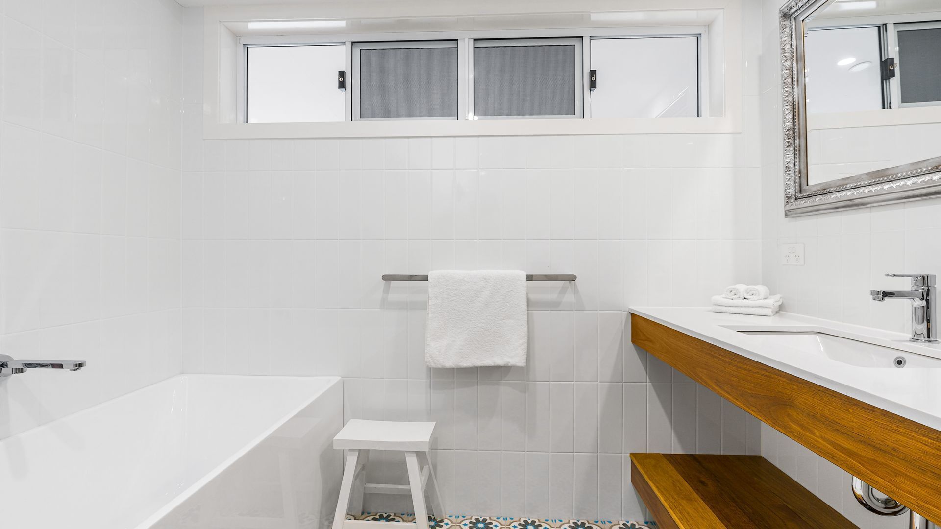 A modern bathroom with a white bathtub, a wooden vanity, and a small stool.
