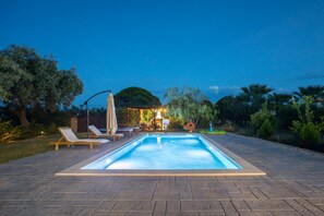 A rectangular swimming pool with a tiled deck, surrounded by lounge chairs and a covered seating area. - Artemis Stone Villa (Zakynthos)