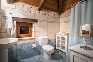 A bathroom with a stone wall, wooden beams, a white sink, a toilet, and a mirror. - Artemis Stone Villa (Zakynthos)