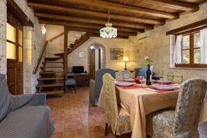 A dining area with a table set for four, wooden chairs, a chandelier, and a staircase leading to another room. - Artemis Stone Villa (Zakynthos)