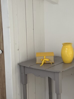 Uma pequena mesa com um vaso amarelo e uma caixa de presente em frente a uma parede branca.