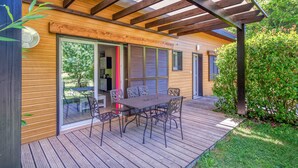 Una terraza de madera con mesa y sillas, una pérgola y un ventanal que da a un patio.