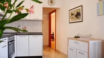 Eine moderne Küche mit weißen Schränken, einem Edelstahlbackofen und einer gefliesten Spritzschutzwand. Eine Holztür führt in einen anderen Raum, und ein gerahmtes Bild ist an der Wand angebracht.