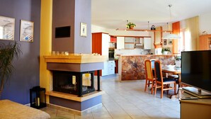 Ein modernes Wohnzimmer mit Kamin, Essbereich und einer Küche im Hintergrund.