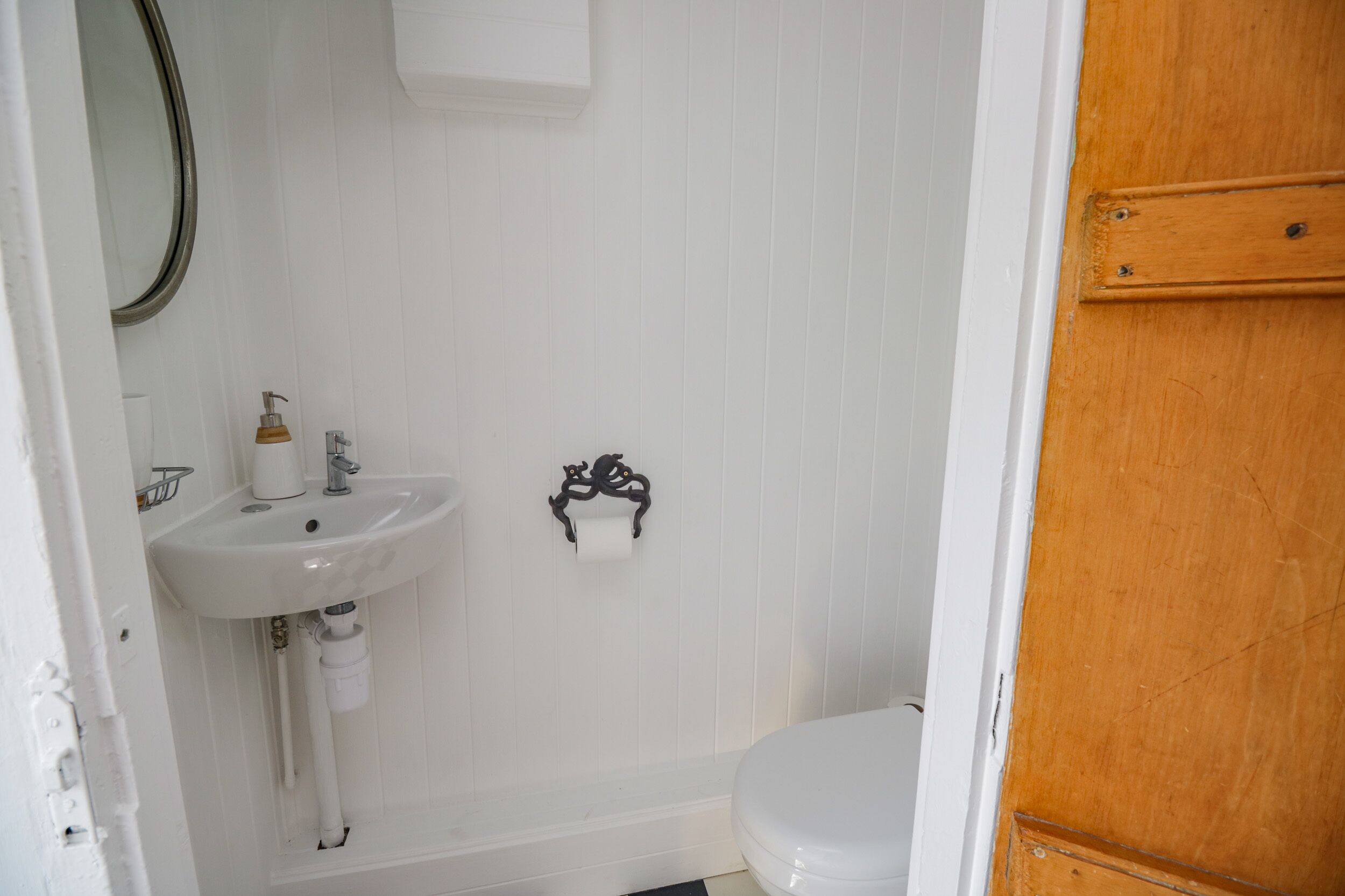 Ein Badezimmer mit einem weißen Waschbecken, einer Toilette und einer Holztür.