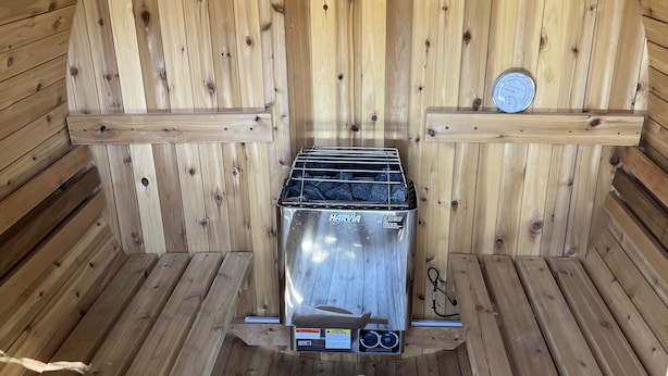 En sauna med Harvia-ovn, træbænke, en træske og et termometer på en hylde.