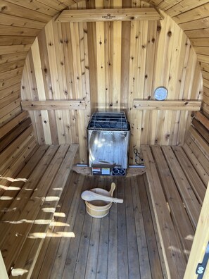 Een sauna met een Harvia-kachel, houten banken, een houten lepel en een thermometer op een plank.