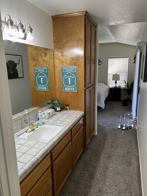 A bathroom with a sink, mirror, and wooden cabinets. There are two signs on the wall indicating directions to Pacific Coast Highway and North. - Cheerful 3BR 2BA Sauna: Spa: Pool/P-Pong Table+ More (Lancaster)
