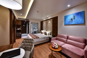 Una habitación de hotel moderna con una cama grande, un sofá rosa, una mesita con flores y un cuadro en la pared.