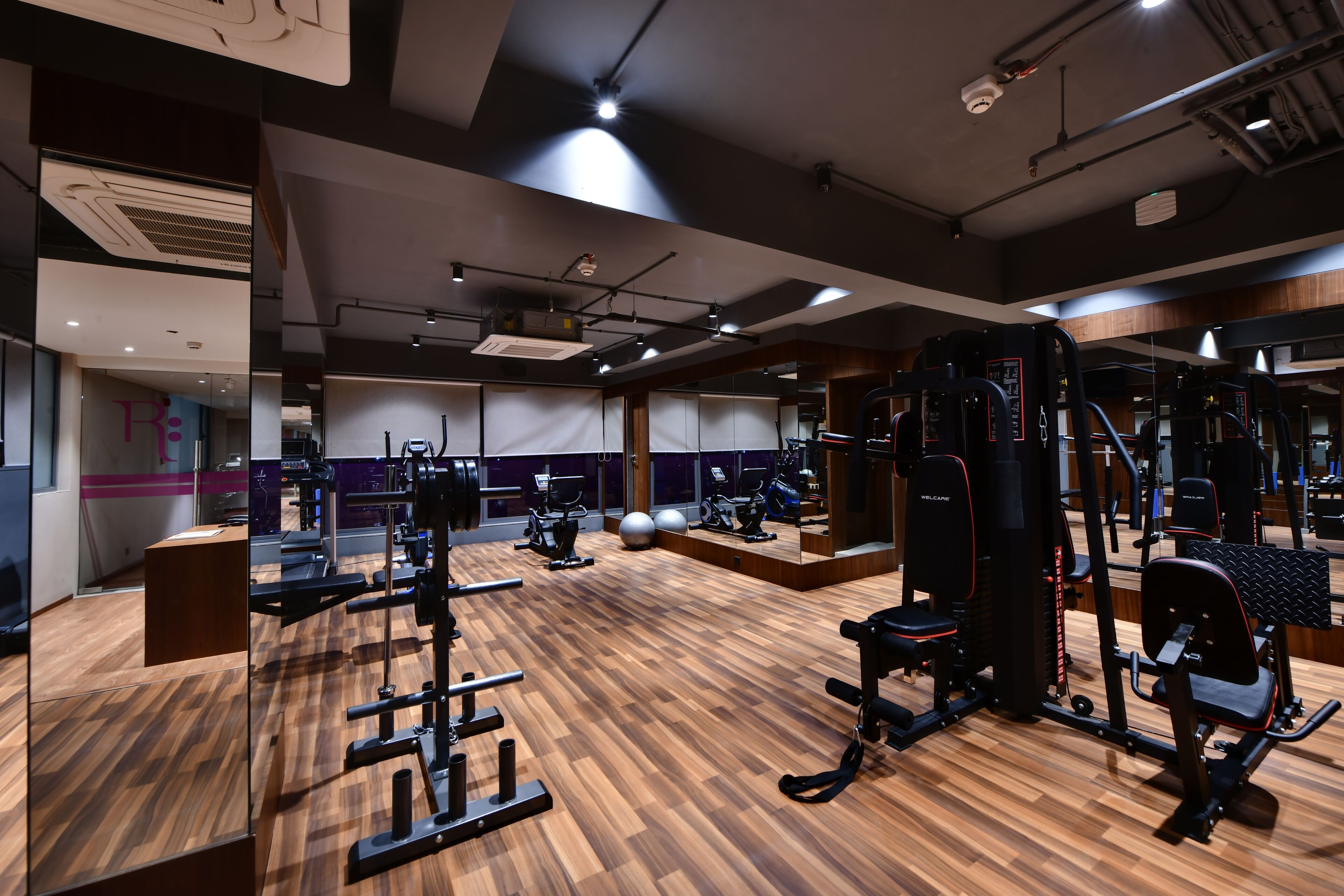 Ett gym med olika typer av träningsredskap, trägolv och speglar.