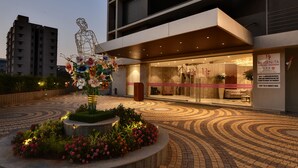 Un edificio moderno con entrada de vidrio, una escultura decorativa y un parterre circular.