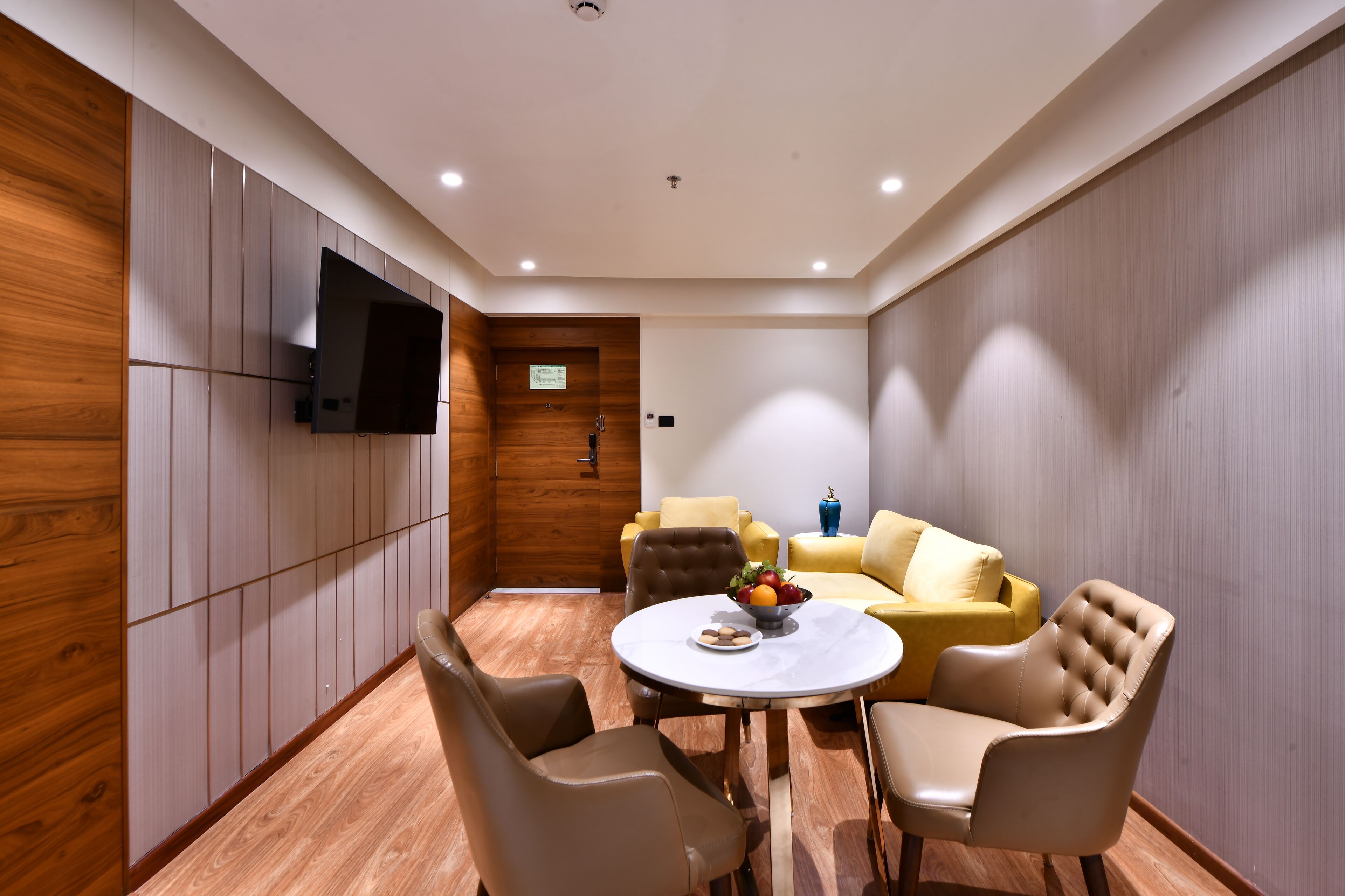 A modern living room with a round table, leather chairs, a yellow sofa, and a flat-screen TV mounted on the wall.
