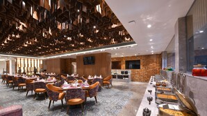 Un comedor amplio con varias mesas y sillas, una barra de buffet con diversos alimentos y un diseño moderno de techo.