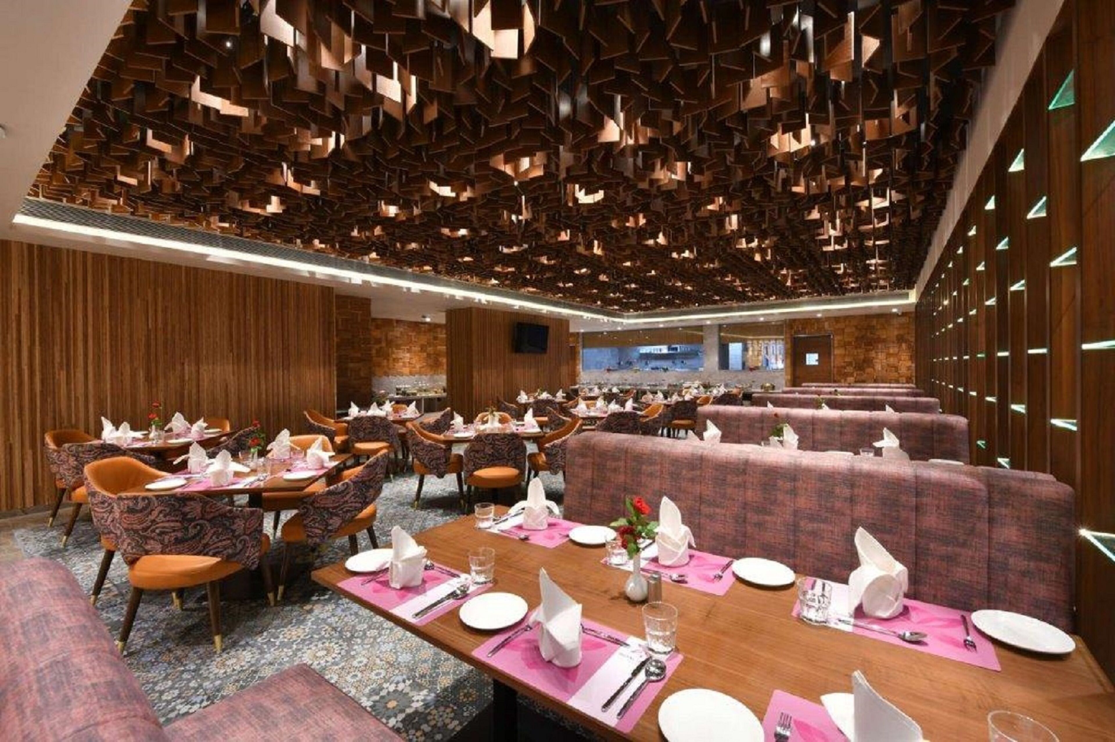Un comedor moderno con varias mesas y cabinas, paneles de madera en las paredes y una alfombra estampada.