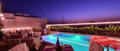 A dining area with tables set for two, overlooking a pool with water features.