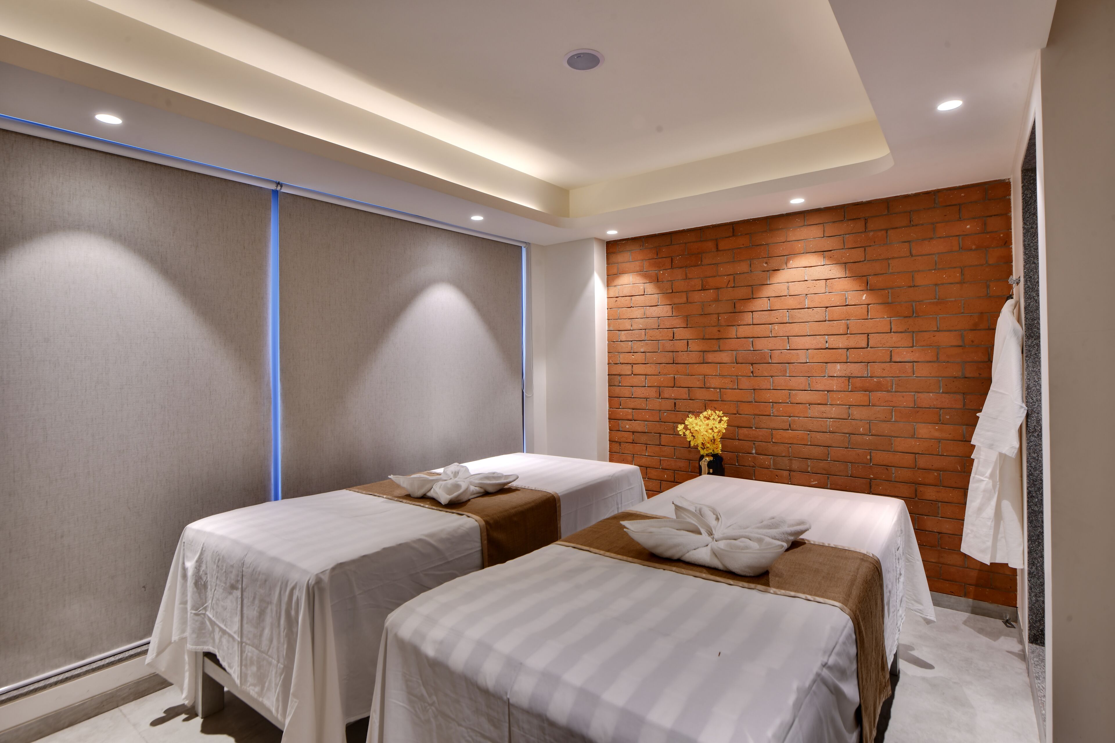 A hotel room with two beds, a brick wall, and a modern ceiling design.
