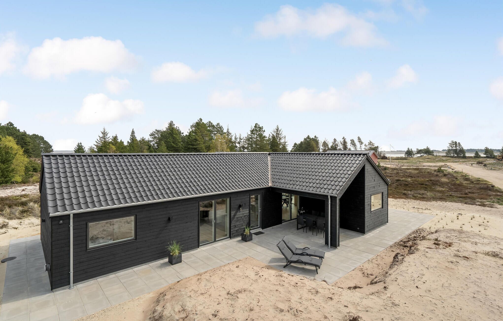 Een modern zwart huis met pannendak, grote ramen en een terras met tuinmeubilair.