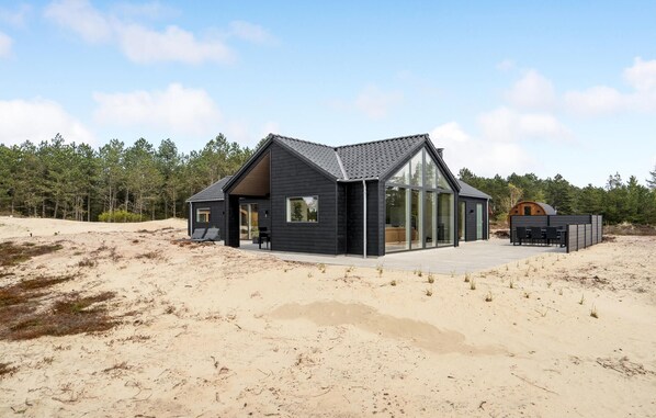A modern beach house with a large glass facade, a covered patio, and a wooden deck.