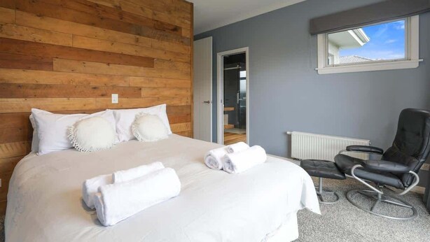 Ein Schlafzimmer mit einem hölzernen Kopfteil, einem Bett mit weißer Bettwäsche, einem schwarzen Massagesessel und einem Fenster mit Blick.